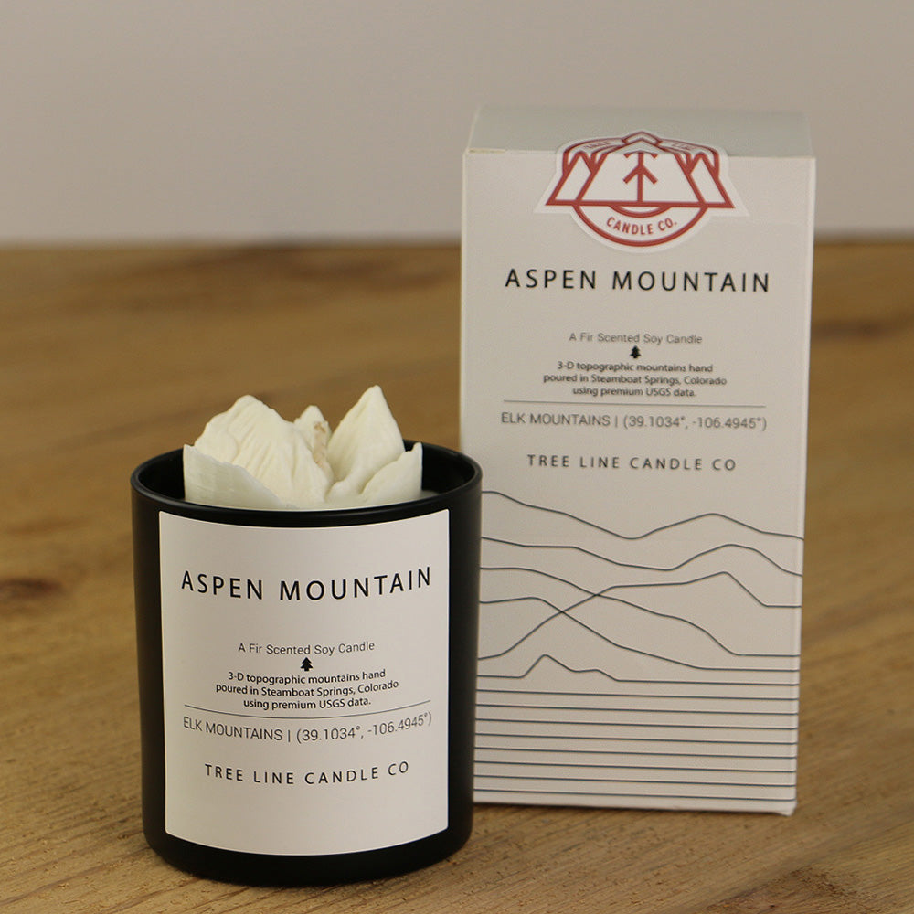 A white wax replica candle of Aspen Mountain next to a white box with red and black lettering.