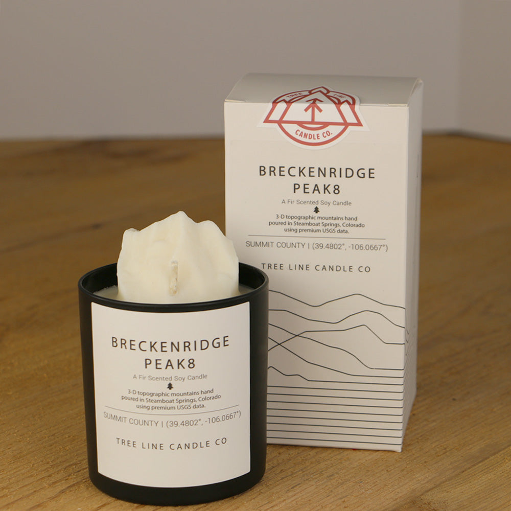  A white wax replica candle of Breckenridge Peak 8 next to a white box with red and black lettering.