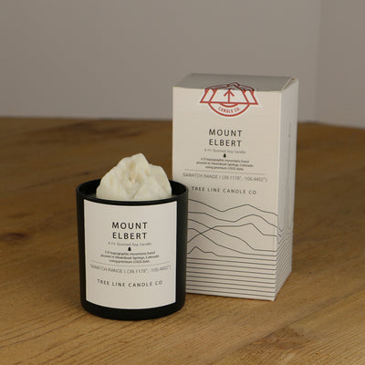 A white wax replica candle of Mount Elbert next to a white box with red and black lettering.