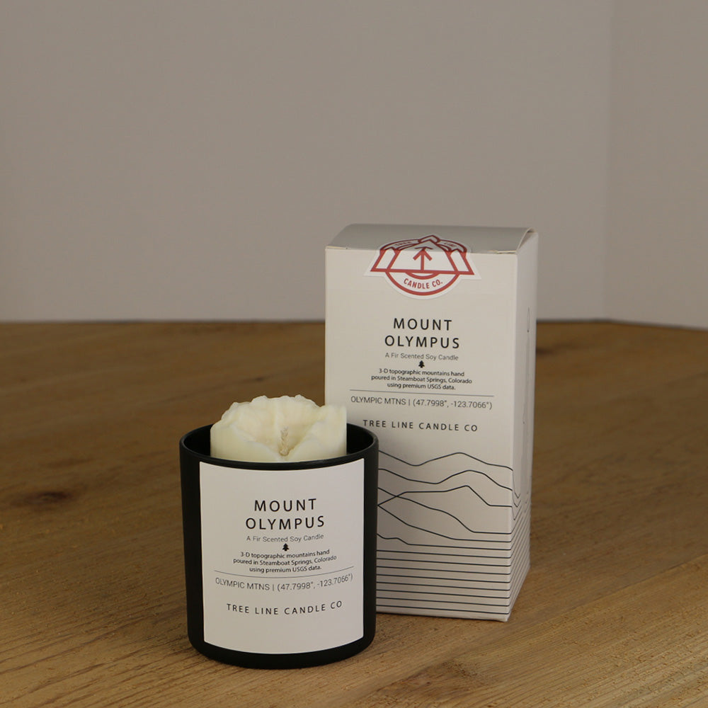 A white wax replica candle of Mount Olympus, WA next to a white box with red and black lettering.