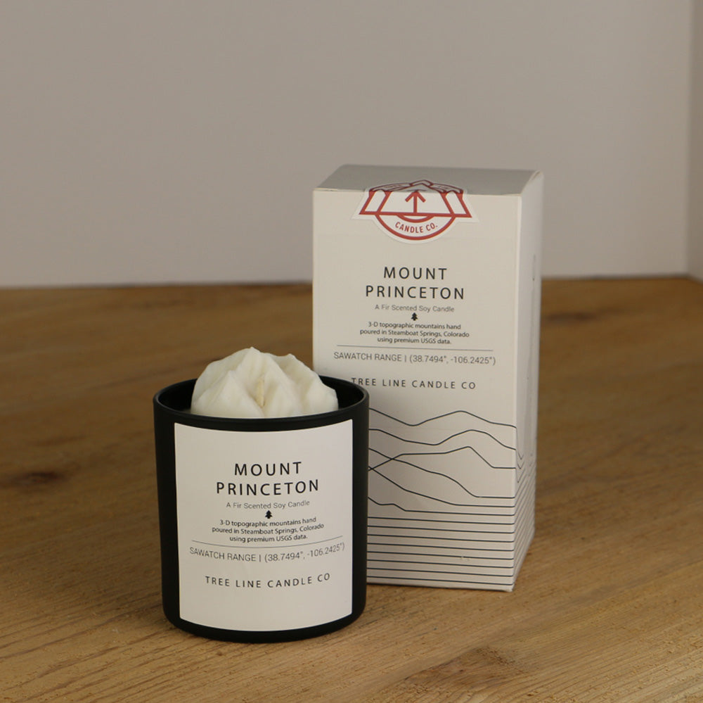 A white wax replica candle of Mount Princeton next to a white box with red and black lettering.