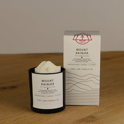 A white wax replica candle of Mount Rainier next to a white box with red and black lettering.