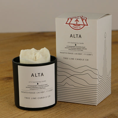 A white wax replica candle of Alta mountain next to a white box with red and black lettering.