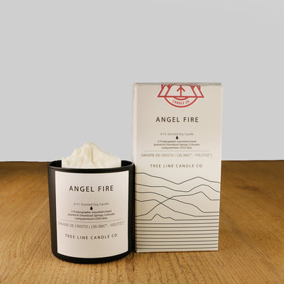 A white wax candle named Angel Fire is next to a white box with red and black lettering.