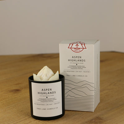 A white wax replica candle of Aspen Highlands next to a white box with red and black lettering.