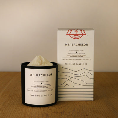 A white wax candle named Mount Bachelor is next to a white box with red and black lettering.