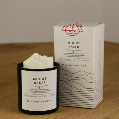 A white wax replica candle of Mount Baker next to a white box with red and black lettering.