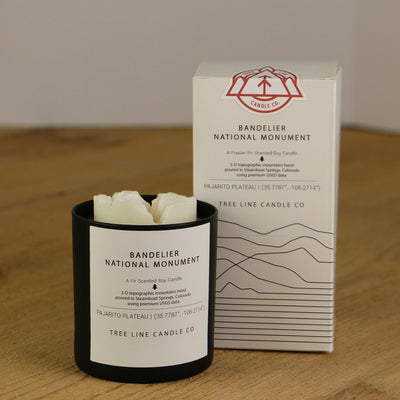 A white wax replica candle of Bandelier National Monument next to a white box with red and black lettering.