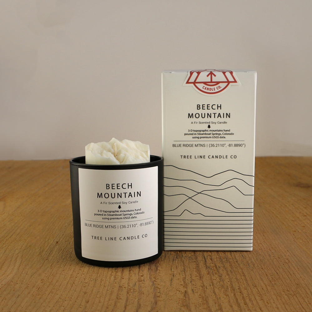 A white wax candle named  Beech Mountain is next to a white box with red and black lettering.