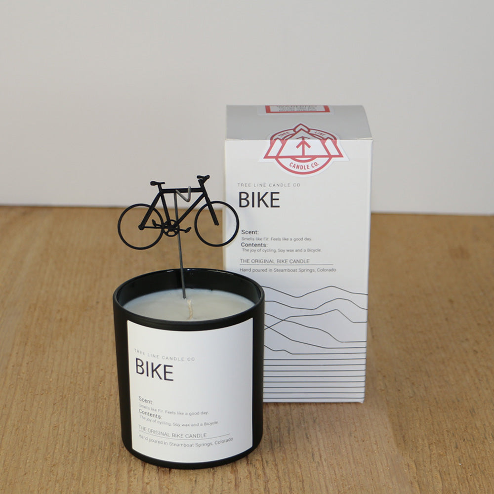 A white wax  candle named Bike next to a white box with red and black lettering.