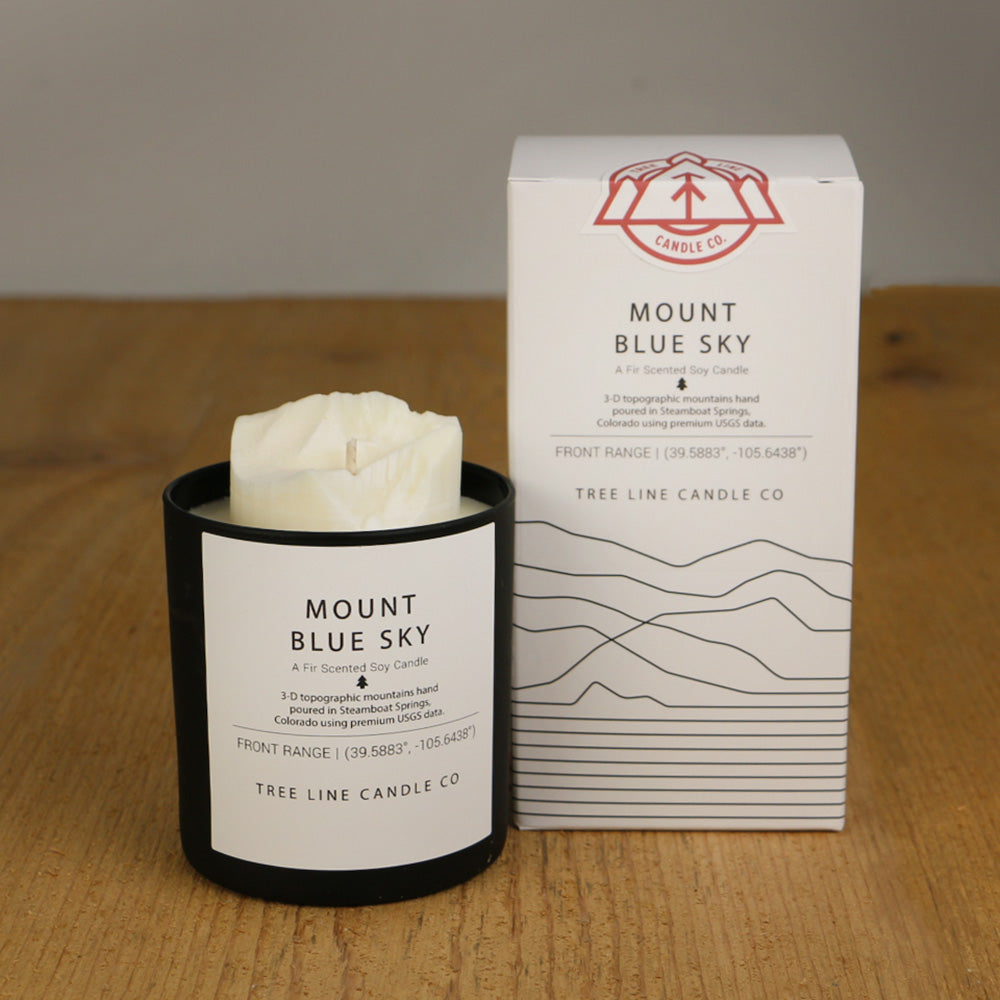 A white wax candle named Mount Blue Sky is next to a white box with red and black lettering.