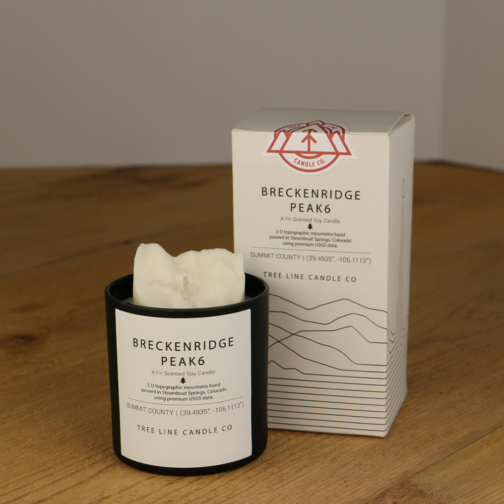  A white wax replica candle of Breckenridge Peak 6 next to a white box with red and black lettering.