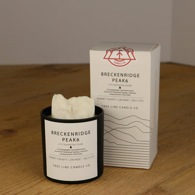 A white wax replica candle of Breckenridge Peak 6 next to a white box with red and black lettering.