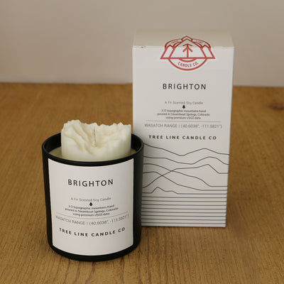 A white wax candle named Brighton is next to a white box with red and black lettering.