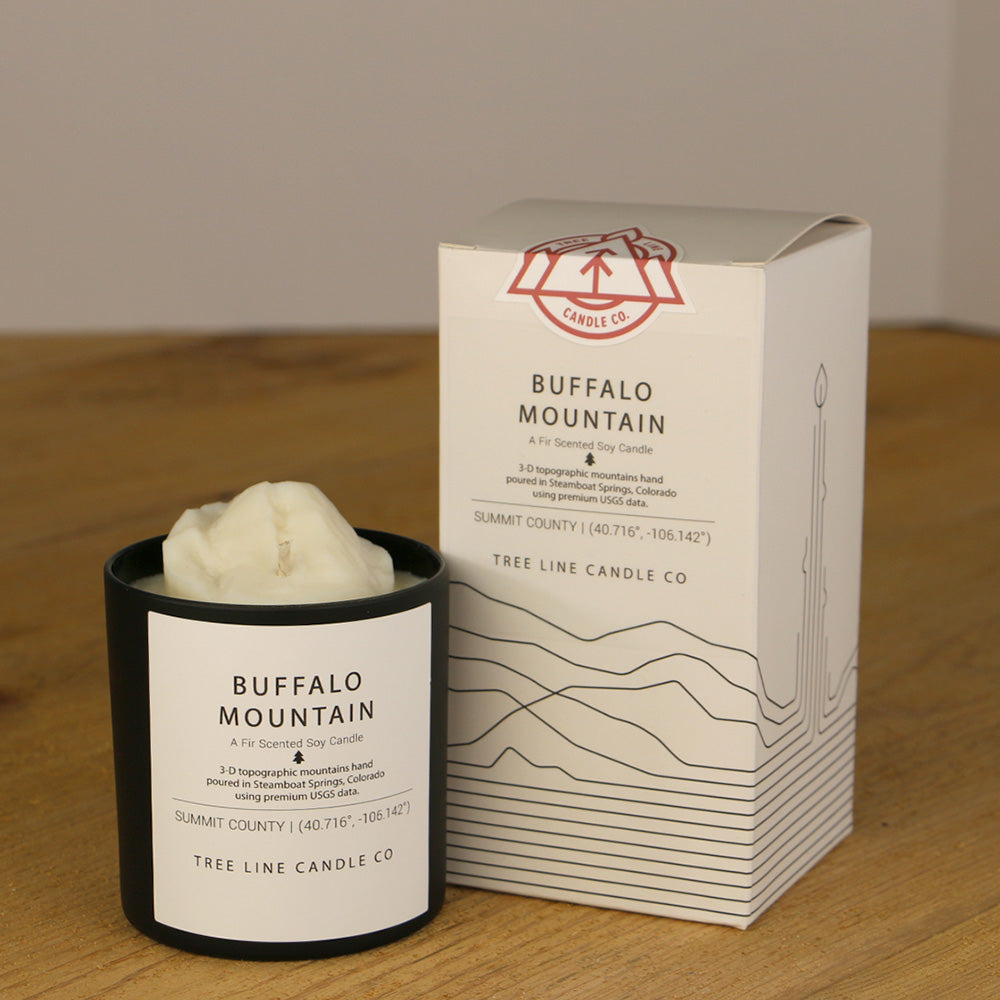 A white wax replica candle of Buffalo Mountain next to a white box with red and black lettering.