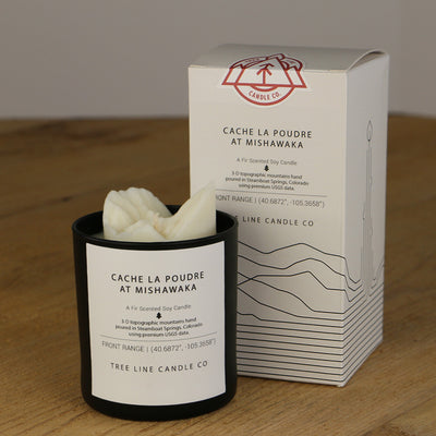 A white wax replica candle of Cache La Poudre At Mishawaka next to a white box with red and black lettering.