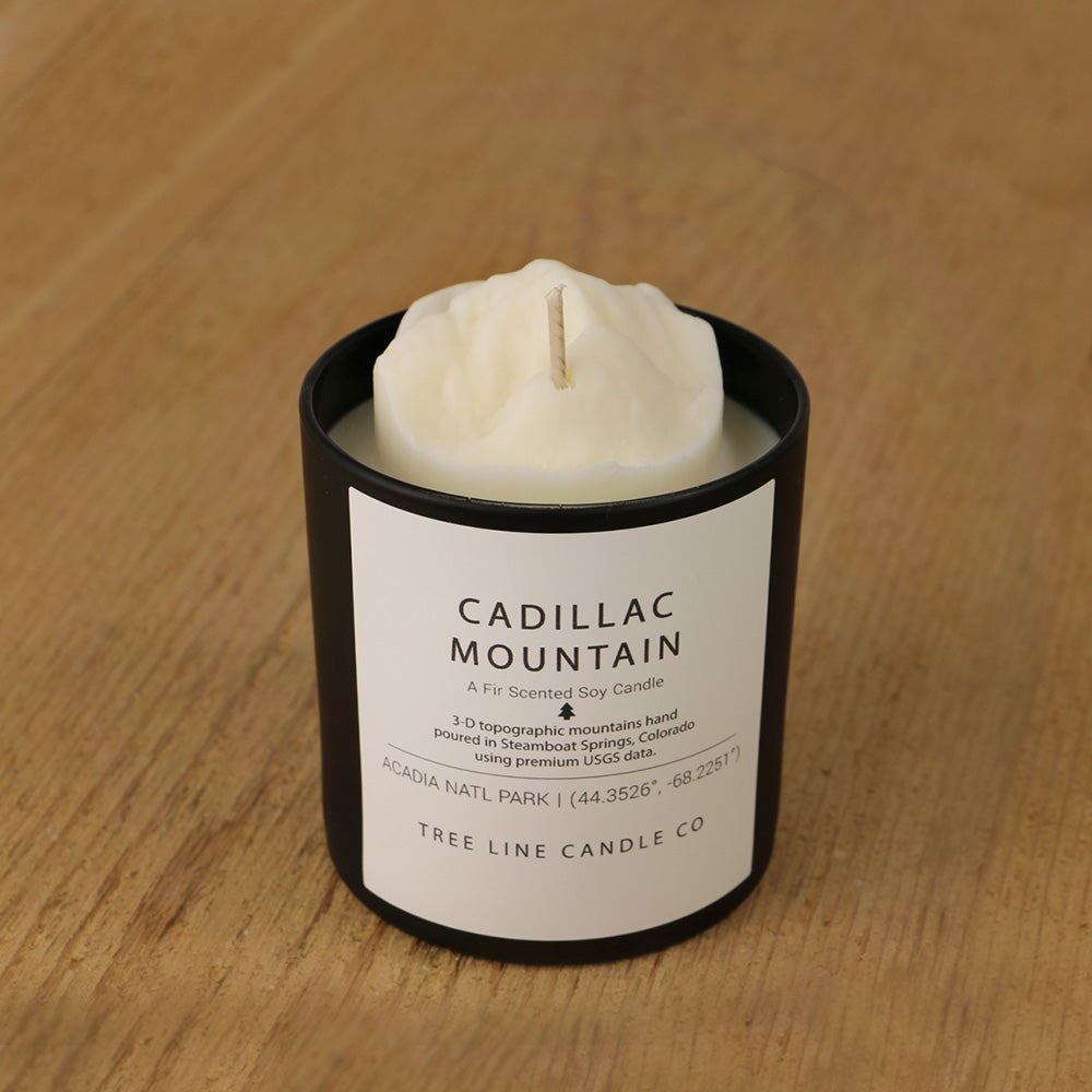  A white soy wax replica candle of Cadillac Mountain in a round, black glass.