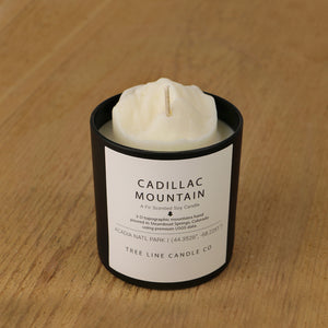  A white soy wax replica candle of Cadillac Mountain in a round, black glass.