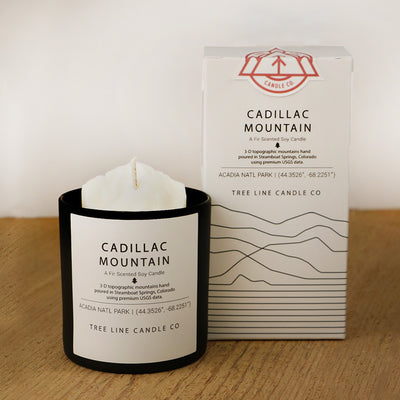 A white wax candle named Cadillac Mountain is next to a white box with red and black lettering.