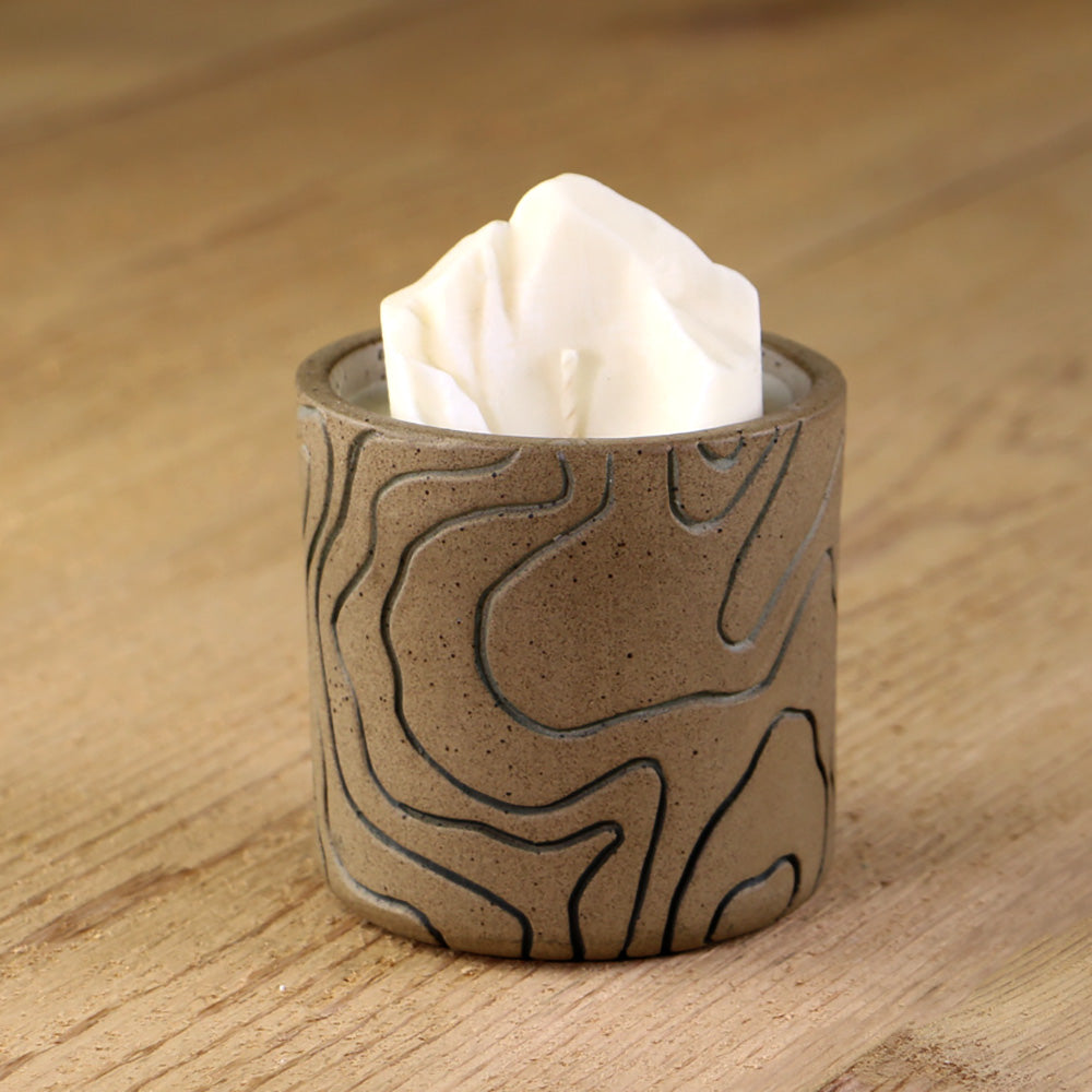 A white soy wax candle replica of Longs Peak in a decorative ceramic base inlaid with gray lines.