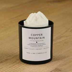 A white soy wax replica candle of Copper Mountain in a round, black glass.