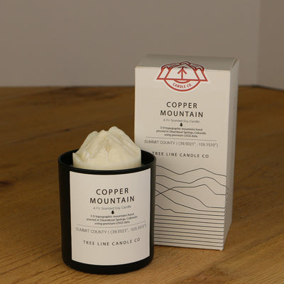 A white wax replica candle of Copper Mountain next to a white box with red and black lettering.