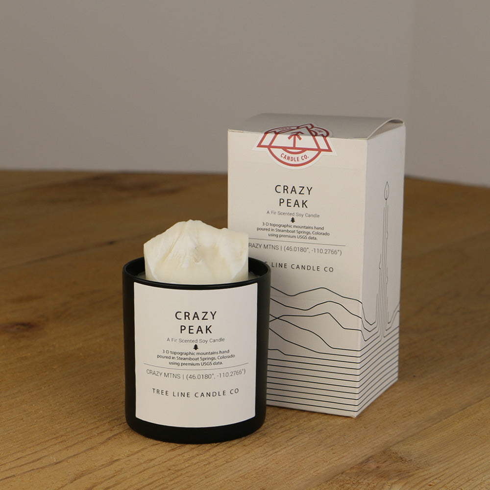 A white wax replica candle of Crazy Peak next to a white box with red and black lettering.