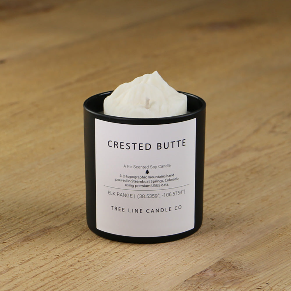 A white soy wax replica candle of Crested Butte in a round, black glass.