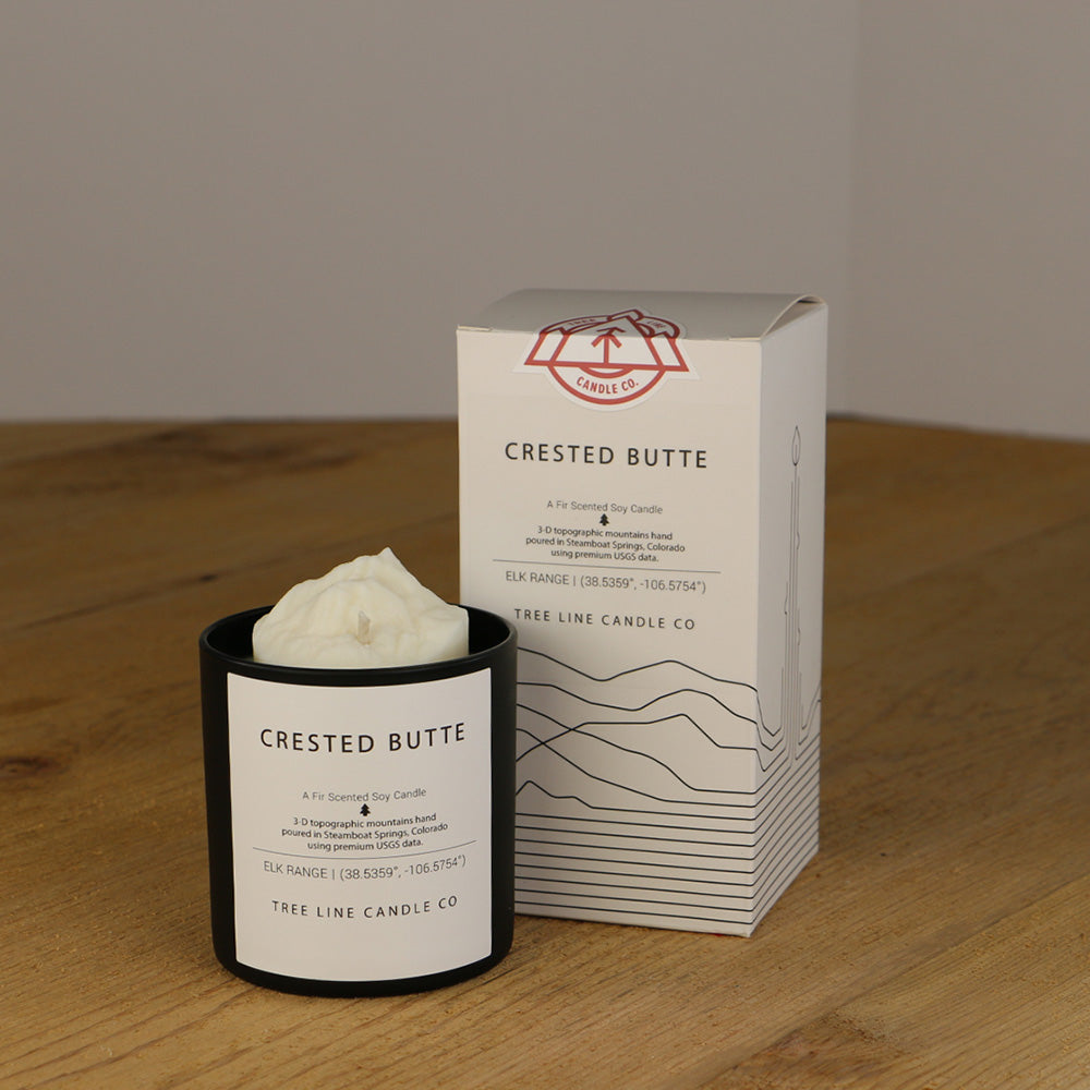 A white wax replica candle of Crested Butte next to a white box with red and black lettering.