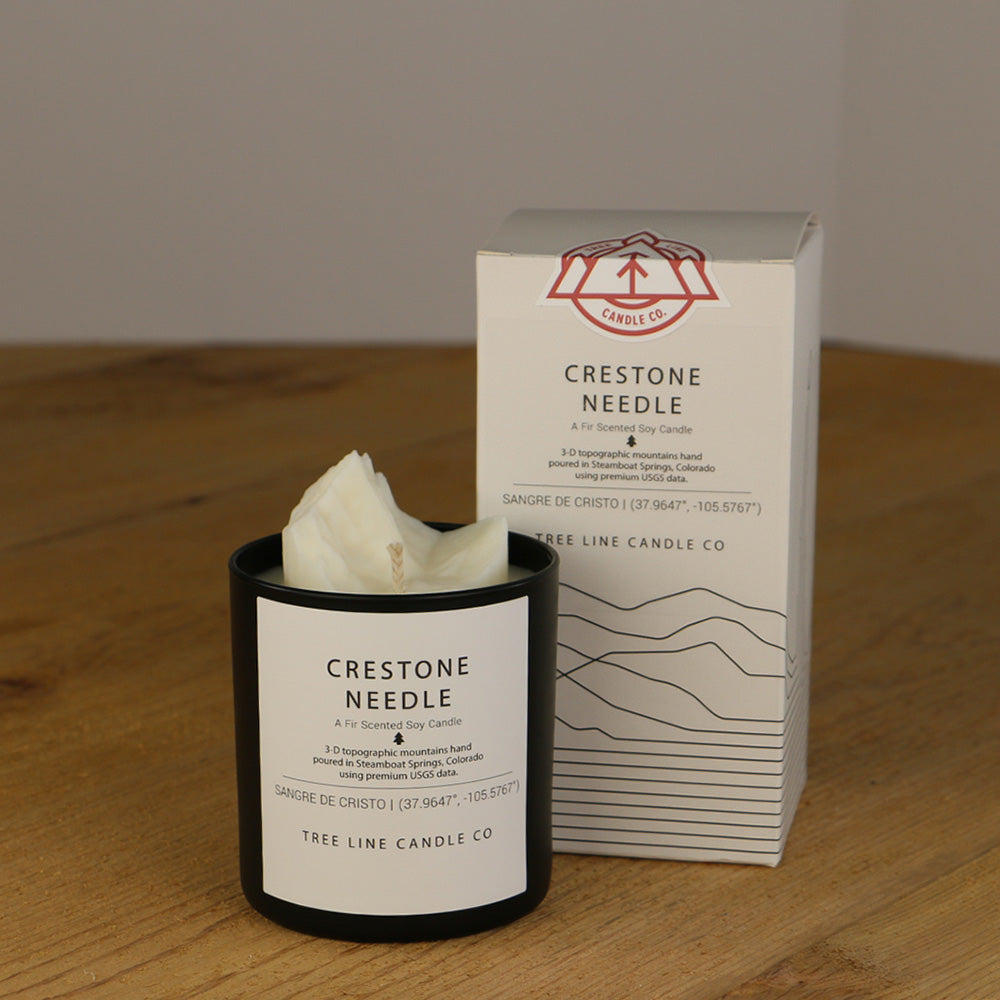 A white wax replica candle of Crestone Needle next to a white box with red and black lettering.