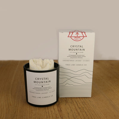 A white wax candle named Crystal Mountain is next to a white box with red and black lettering.