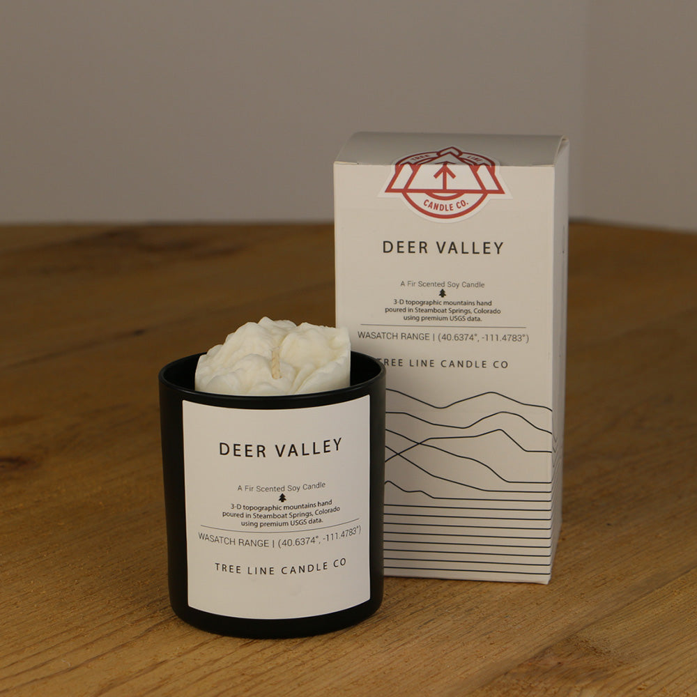 A white wax replica candle of Deer Valley next to a white box with red and black lettering.