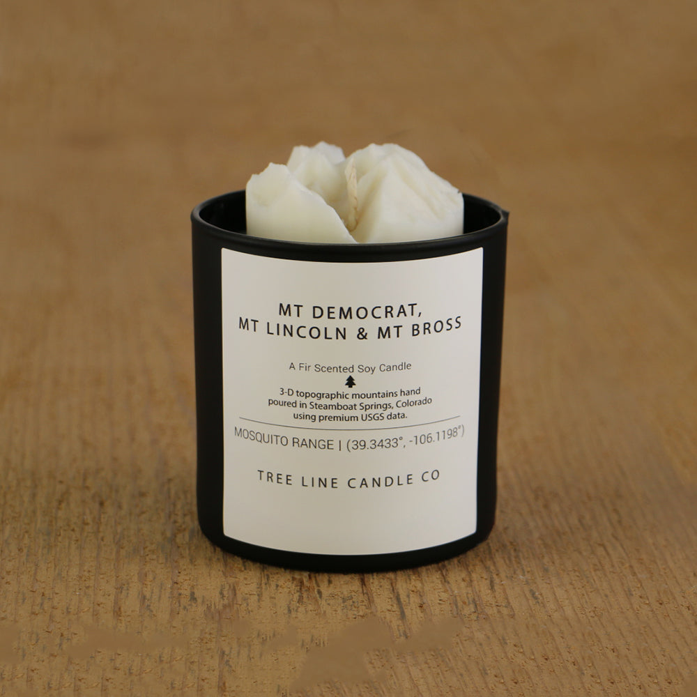 A white soy wax replica candle of Mt. Democrat, Mt. Lincoln & Mt Bross in a round, black glass.