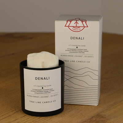 A white wax replica candle of Denali summit next to a white box with red and black lettering.