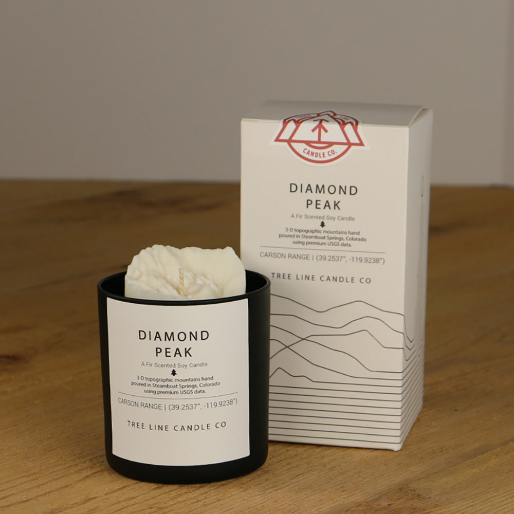A white wax replica candle of Diamond Peak next to a white box with red and black lettering.