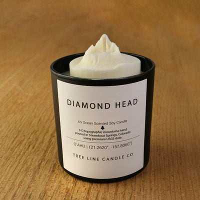 A white soy wax replica candle of Diamond Head in a round, black glass.
