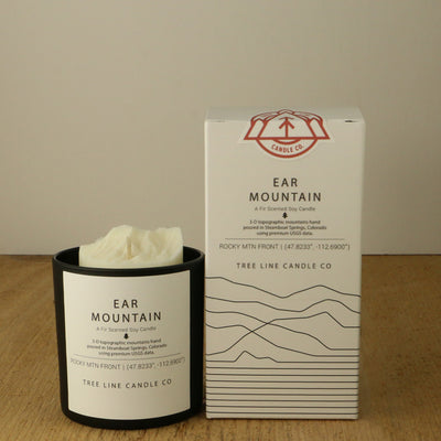 A white wax candle named Ear Mountain is next to a white box with red and black lettering.