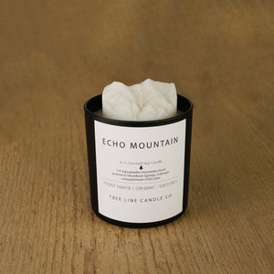 A white soy wax replica candle of Echo Mountain in a round, black glass.