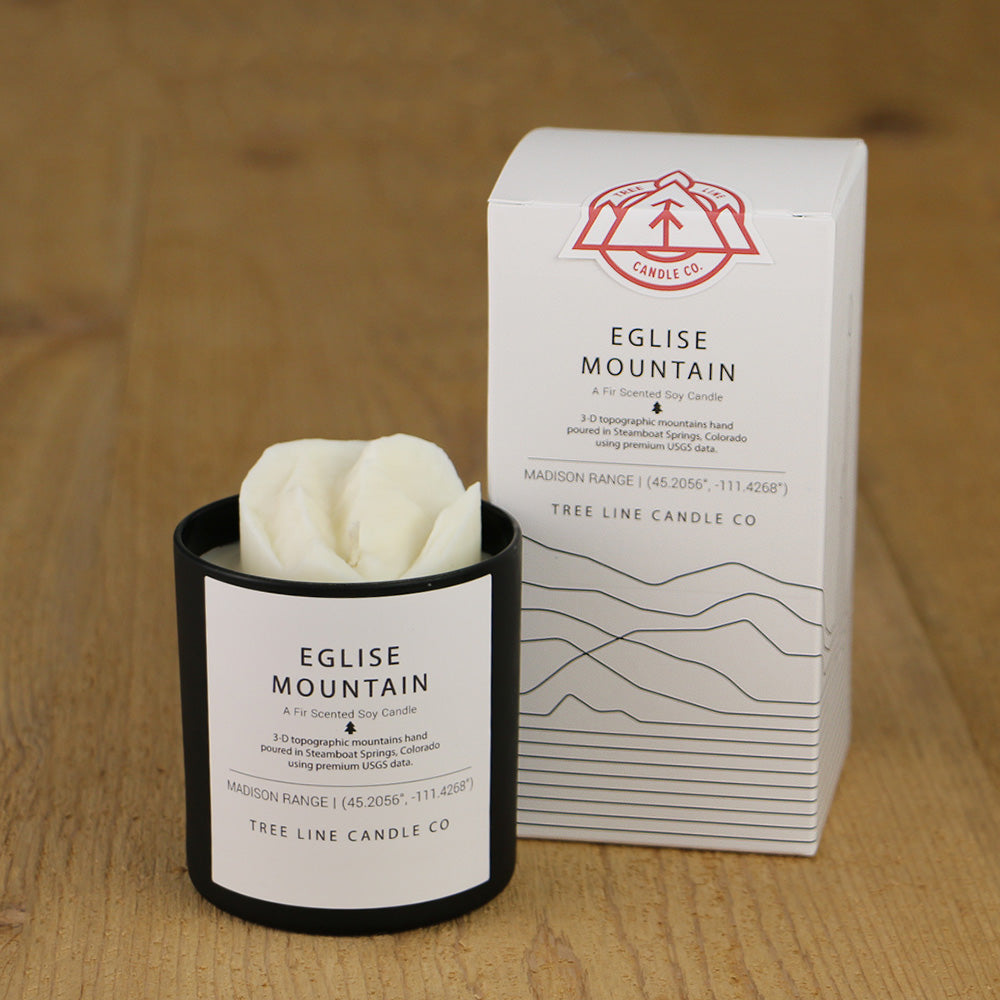 A white wax candle named Eglise Mountain is next to a white box with red and black lettering.