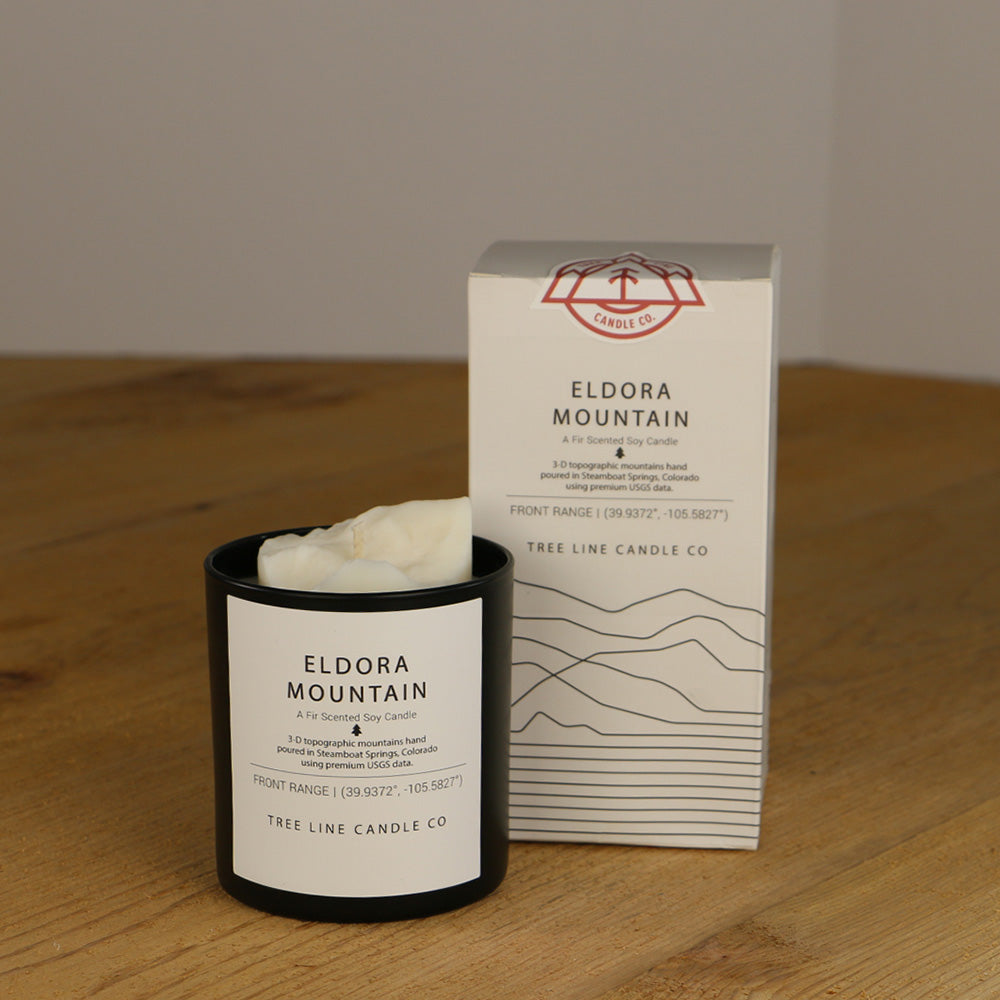 A white wax replica candle of Eldora Mountain next to a white box with red and black lettering.