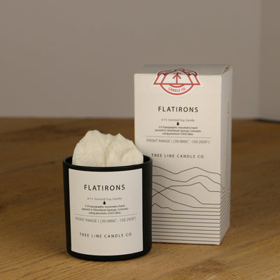 A white wax replica candle of Flatirons next to a white box with red and black lettering.