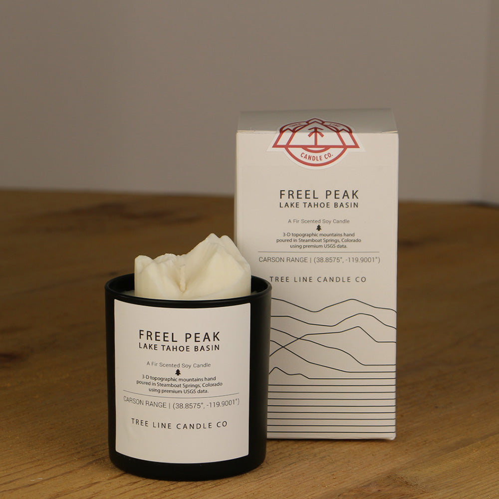 A white wax replica candle of Freel Peak Lake Tahoe Basin next to a white box with red and black lettering.