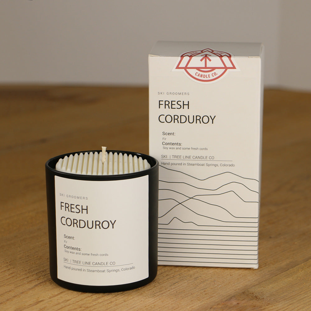 A white wax replica candle of Fresh Corduroy next to a white box with red and black lettering.