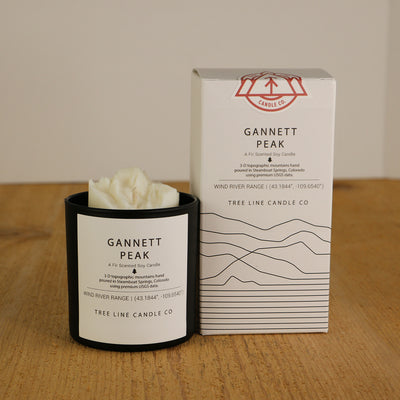 A white wax candle named Gannett Peak is next to a white box with red and black lettering.