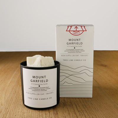 A white wax candle named Mount Garfield is next to a white box with red and black lettering.