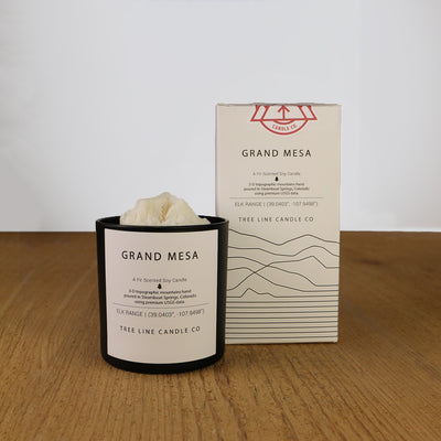 A white wax candle named Grand Mesa is next to a white box with red and black lettering.