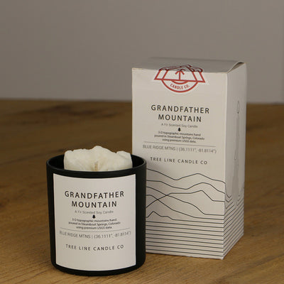 A white wax replica candle of Grandfather Mountain next to a white box with red and black lettering.
