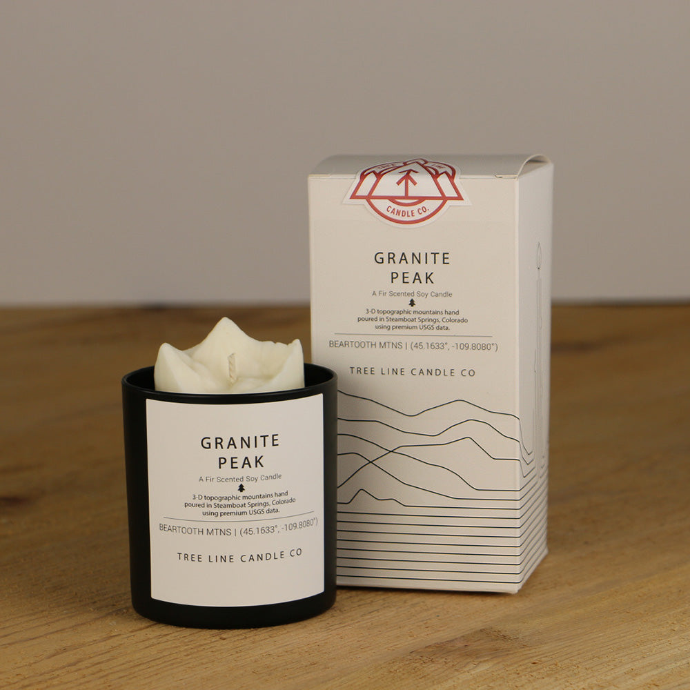 A white wax replica candle of Granite Peak summit next to a white box with red and black lettering.