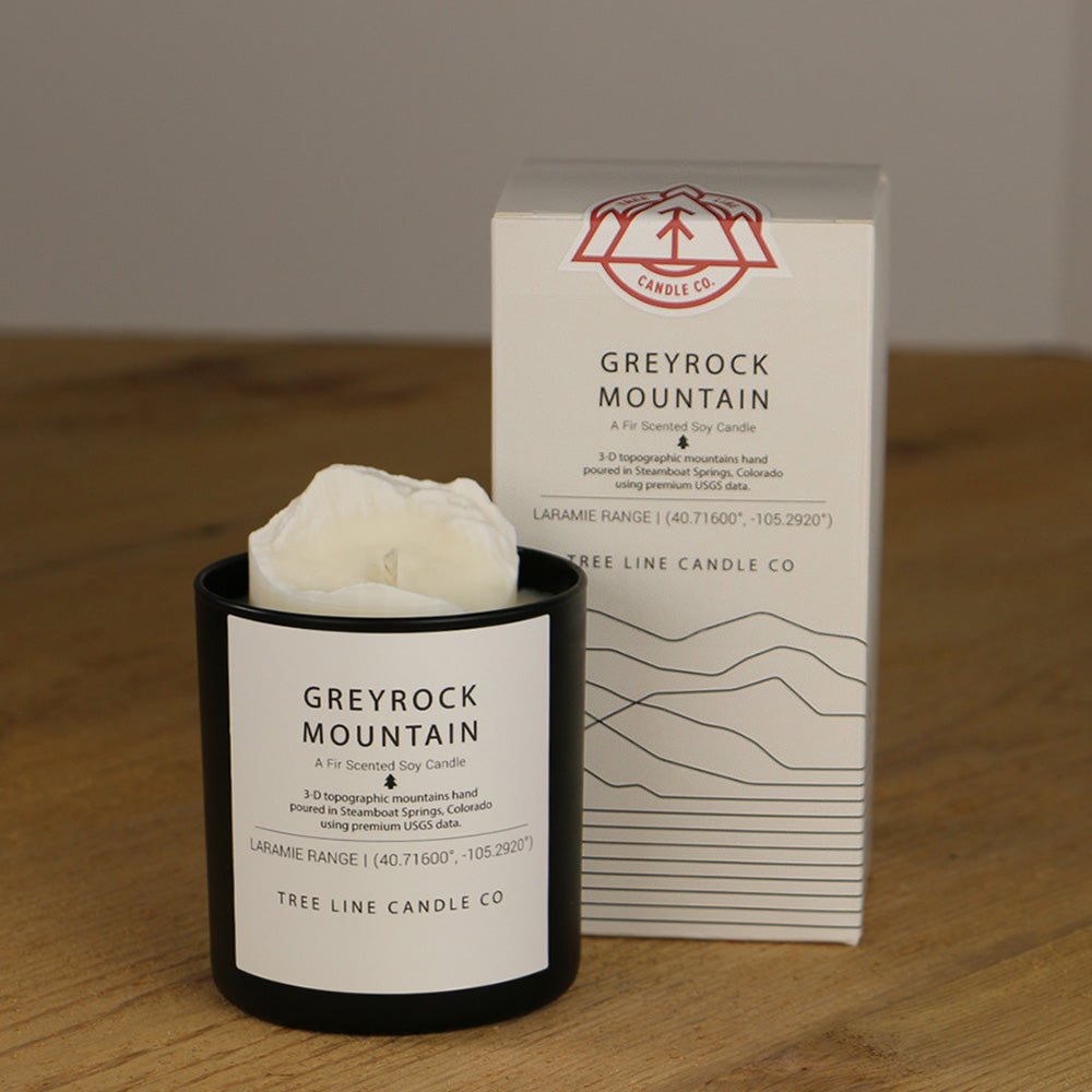 A white wax replica candle of Greyrock Mountain next to a white box with red and black lettering.