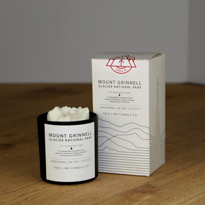 A white wax replica candle of Mount Grinnell Glacier National Park next to a white box with red and black lettering.